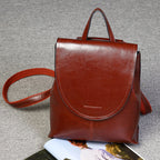 A glossy brown genuine leather retro women’s backpack with a top handle, flap closure, and adjustable straps.