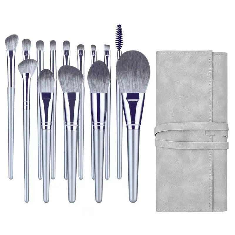 A set of grey makeup brushes with soft bristles, metallic handles, and a matching grey roll-up storage pouch.