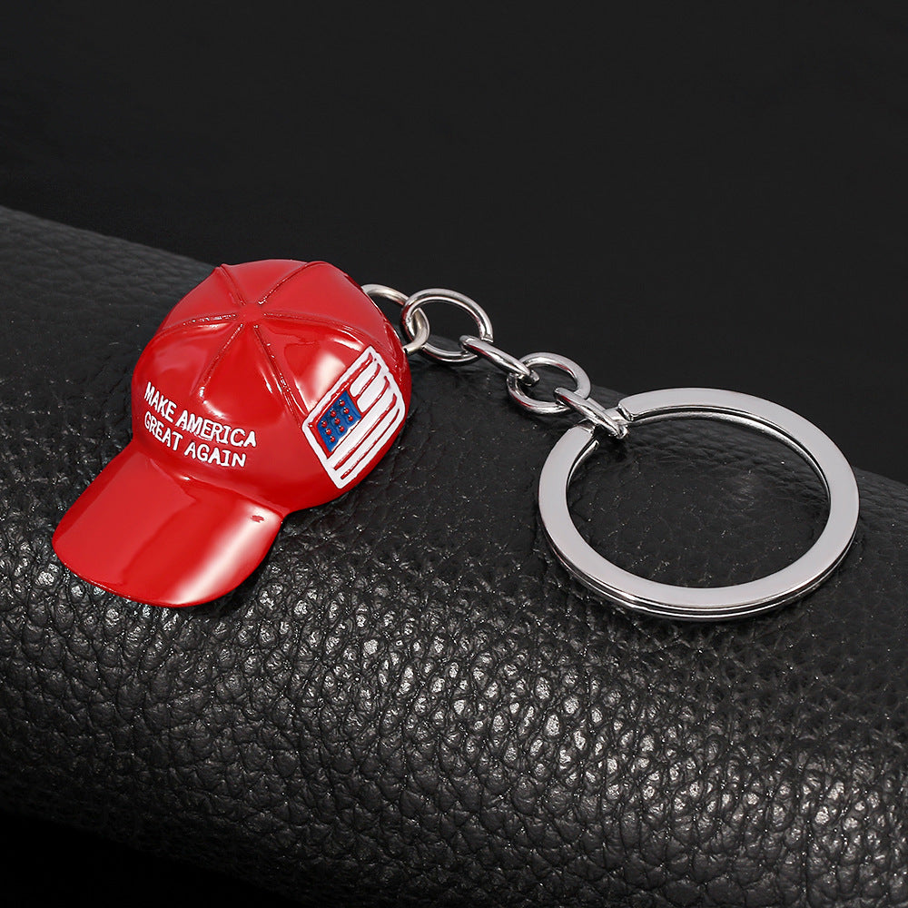 Red enamel baseball cap keychain with "MAKE AMERICA GREAT AGAIN" text, a flag emblem, and a silver metal ring.