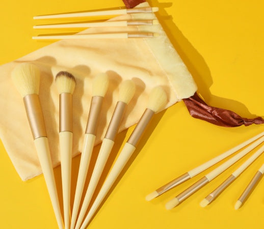 13-piece cream and gold makeup brush set with a soft velvet pouch on a bright yellow background.