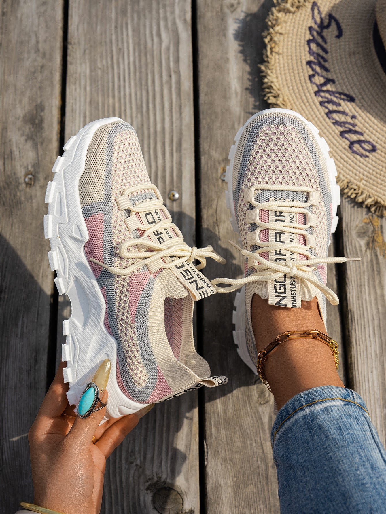 Beige and pink knit mesh lace-up sneakers with thick white soles, held over a wooden deck.