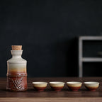 Ceramic sake set with bamboo-style carafe, cork stopper, and four matching gradient-brown cups on a dark wood table.