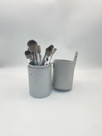 A set of soft-bristled makeup brushes with silver ferrules inside a matching grey cylindrical leather case.