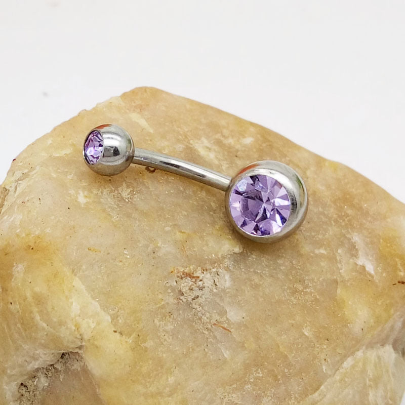 Hypoallergenic titanium steel belly ring with lavender purple crystal stones, resting on a textured beige stone.