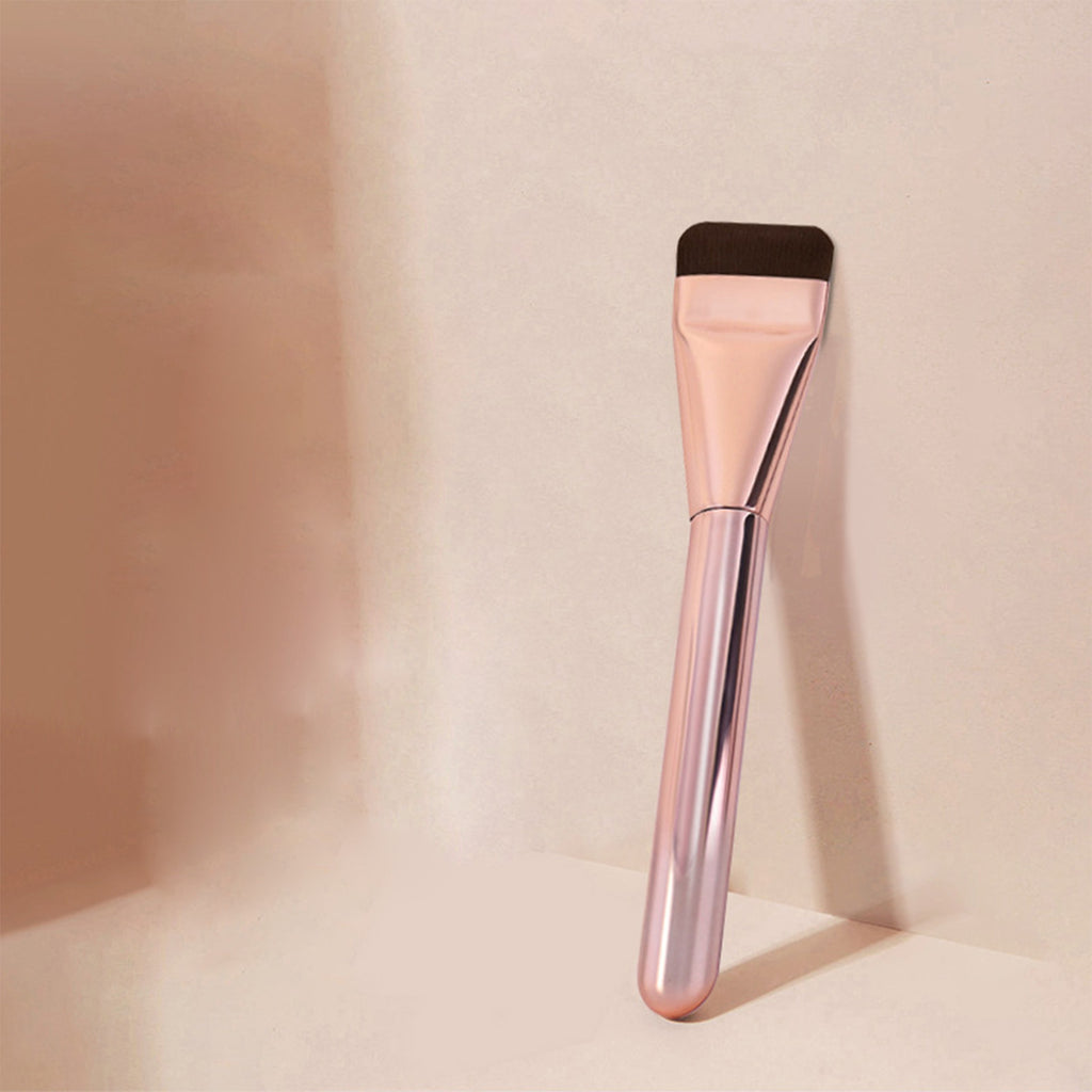 Ultra-thin, flat foundation brush with a metallic rose gold handle and dark brown bristles against a beige background.