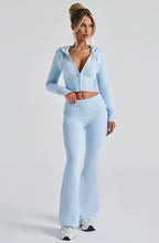 Model wears a slim-fit, powder blue knit set with a cropped, zip-up hooded jacket and matching high-waisted flare pants.