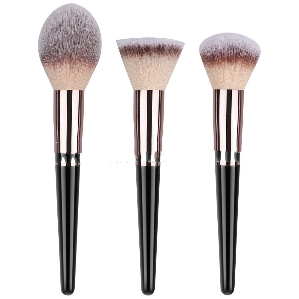 Three makeup brushes with black handles, metallic rose-gold ferrules, and soft, two-toned synthetic bristles.
