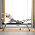 A woman in pink top and grey leggings does pilates on a foldable, black and metallic commercial reformer core bed.