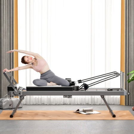 A woman in pink top and grey leggings does pilates on a foldable, black and metallic commercial reformer core bed.