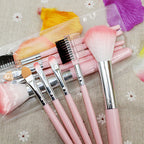 Set of 5 pink makeup brushes with silver ferrules and clear storage pouch on a floral background.