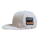 Light gray fabric baseball cap with a black Bluetooth control patch featuring orange playback buttons.