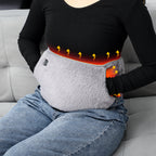 A person wears a grey, plush electric heating stomach belt with a power button, showing heat diffusion graphics.
