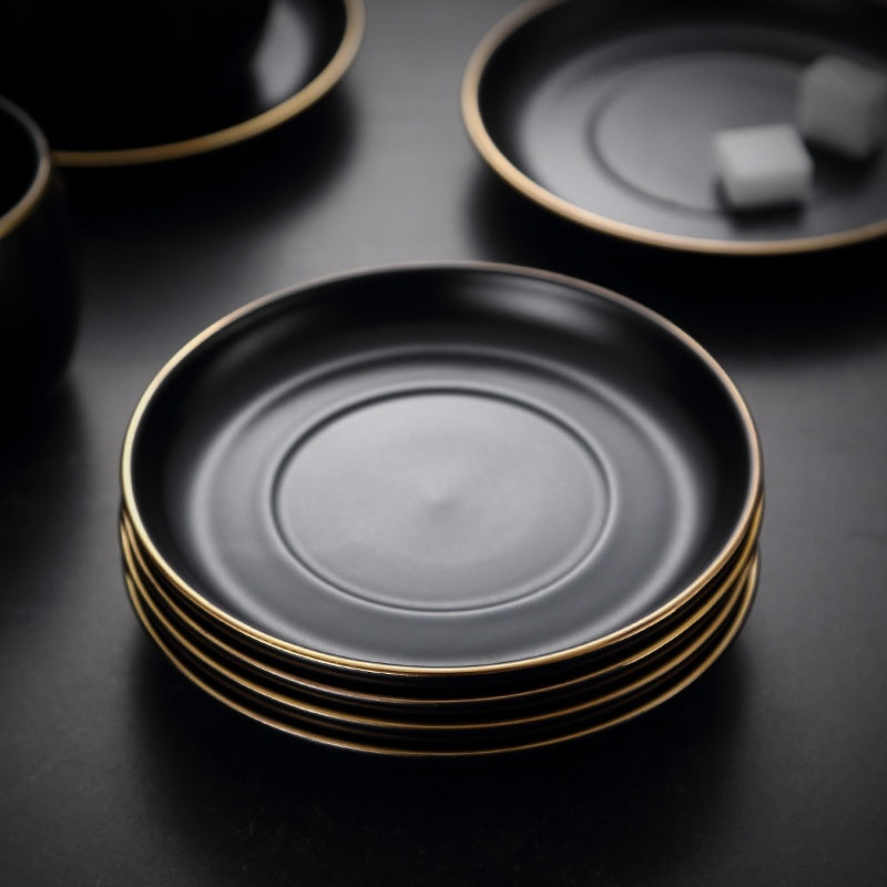 Stack of matte black ceramic saucers with elegant gold rims, shown on a matching dark surface.