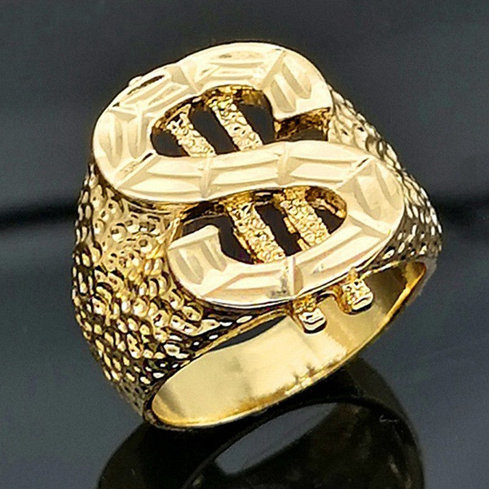 Gold-toned hip hop dollar sign ring with a textured, hammered band design, set against a dark, reflective background.
