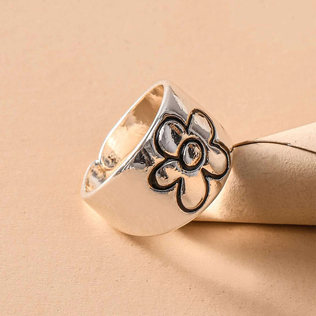 Silver-toned chunky hip-hop ring with a black-outlined flower engraving, set against a neutral beige background.