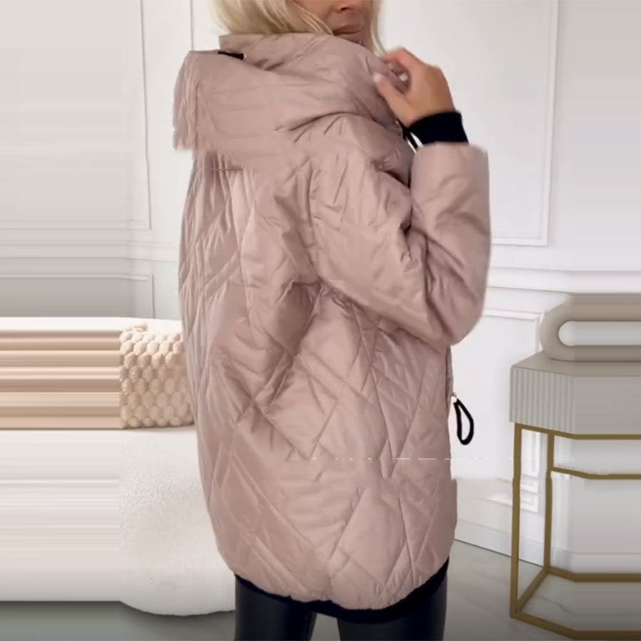 A person wearing a dusty pink, quilted hooded puffer jacket with black sleeve cuffs.