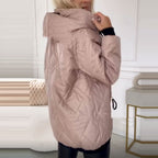 A person wearing a dusty pink, quilted hooded puffer jacket with black sleeve cuffs.