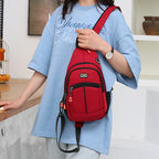 A person wears a red canvas sling backpack with black trim, zippers, a side mesh pocket, and an integrated USB port.
