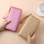 Two glittery, multi-functional clutches in pink and gold with wrist straps, held in hands on a neutral background.