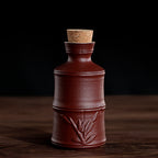 A rustic dark brown ceramic wine bottle with a textured bamboo relief and a cork stopper, set against a dark backdrop.