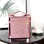 Metallic pink portable makeup bag with top handle, zip closure, and embossed logo on a glass table.