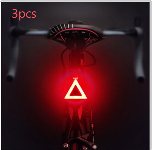 Three triangle-shaped USB bicycle taillights emitting a bright red LED glow, mounted on the back of a bicycle seat.