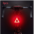 Three triangle-shaped USB bicycle taillights emitting a bright red LED glow, mounted on the back of a bicycle seat.