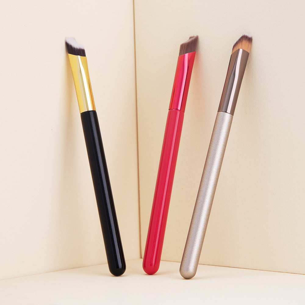 Three angled eyebrow brushes with black, pink, and silver handles against a beige background.