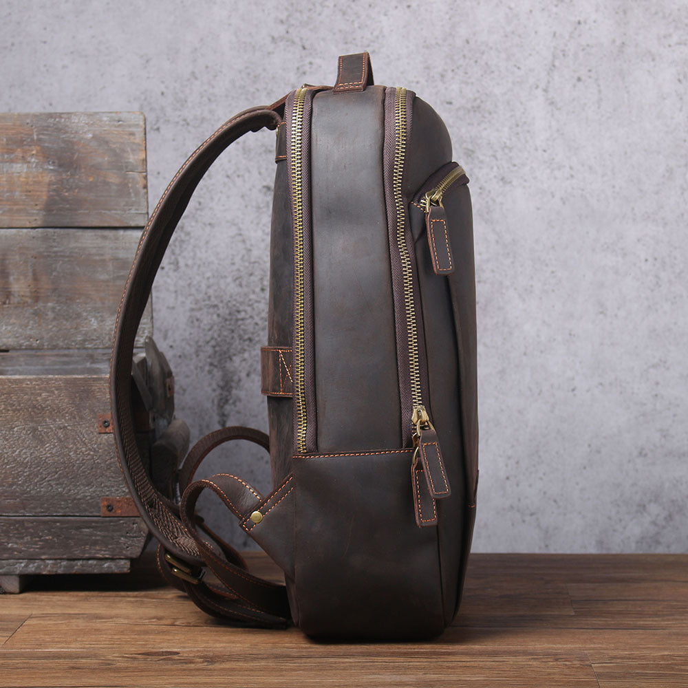 Side view of a brown vintage leather backpack with gold zippers, padded straps, and visible stitched detailing.