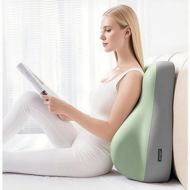 A woman reads while leaning against a contoured, two-tone sage green and grey fabric ergonomic wedge pillow on a bed.