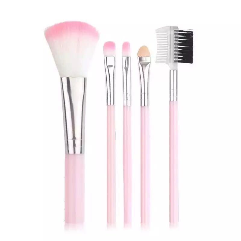 Five makeup brushes with light pink handles, silver ferrules, and soft, white and pink-tipped synthetic bristles.