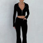 A woman wears a black, ribbed-knit, slim-fit set featuring a long-sleeve, hooded, zip-up crop top and matching pants.