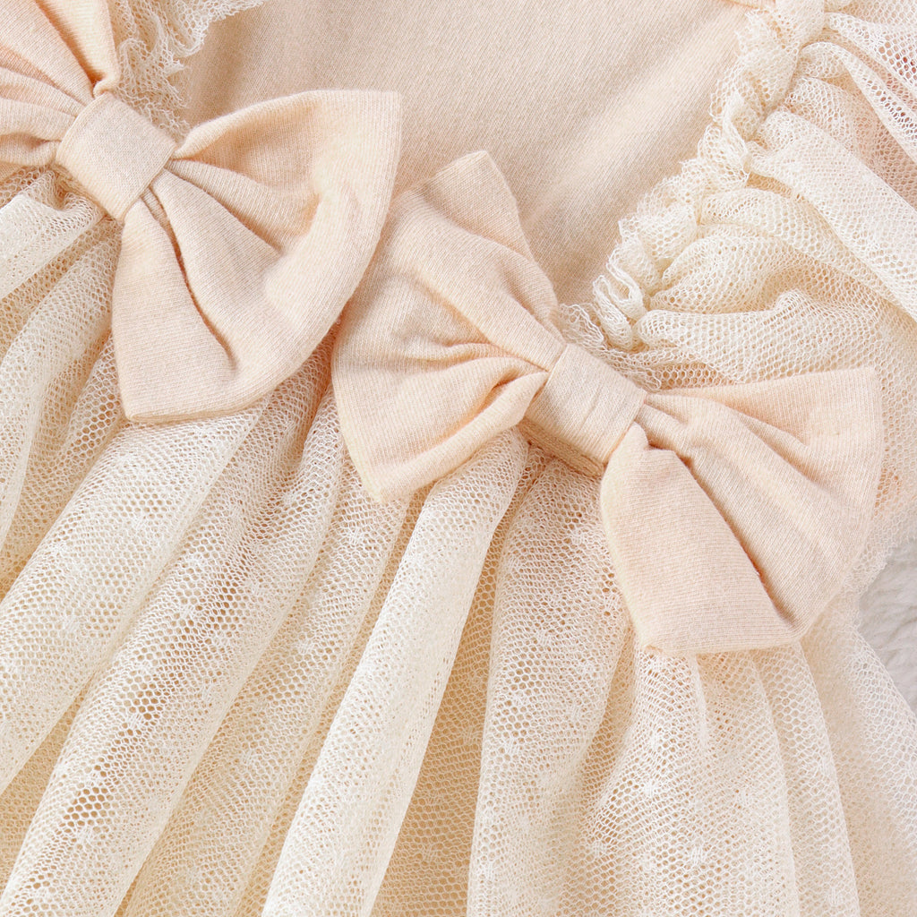 Close-up of a cream baby jumpsuit featuring layered tulle ruffles and soft fabric bows.