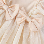 Close-up of a cream baby jumpsuit featuring layered tulle ruffles and soft fabric bows.
