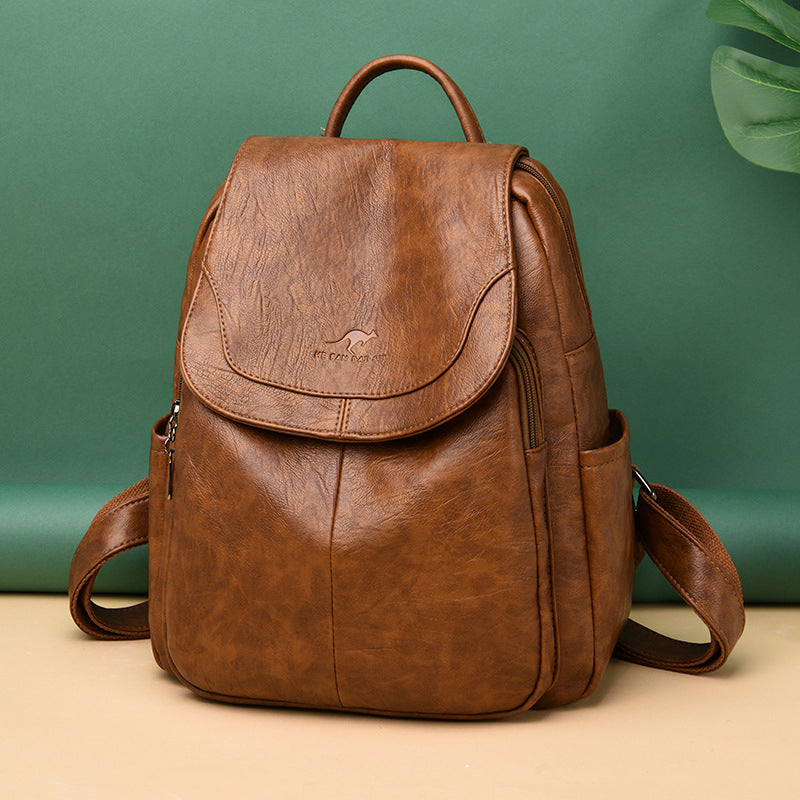 Brown soft leather backpack with a flap closure, kangaroo logo, and top handle against a green background.