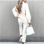 Woman wearing a beige long-sleeve fleece sweater set with matching pants, white sneakers, and a white handbag.