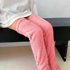 Person wearing thigh-high, plush pink fleece leg warmers while sitting on a black bench.