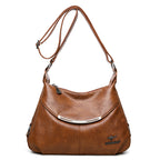 Brown, soft-leather shoulder bag with a curved metallic front accent, top zipper, and kangaroo brand logo.