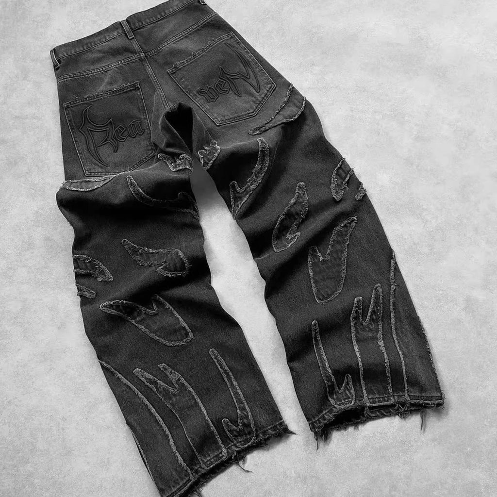 Black baggy denim jeans with frayed flame-shaped patches and gothic embroidery on the back pockets.