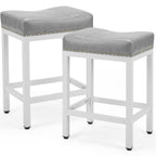 Two grey upholstered saddle bar stools with white steel frames and decorative gold nailhead trim.