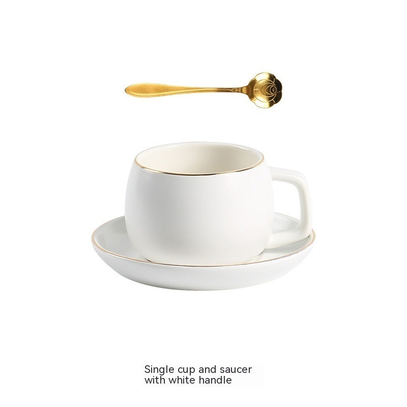 White matte ceramic coffee cup and saucer set with gold-rimmed edges, accompanied by a decorative gold rose spoon.
