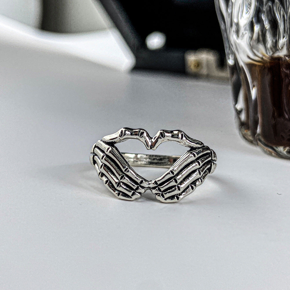 Silver-tone metal ring featuring two skeleton hands forming a heart shape in a gothic, hip-hop style.