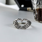 Silver-tone metal ring featuring two skeleton hands forming a heart shape in a gothic, hip-hop style.