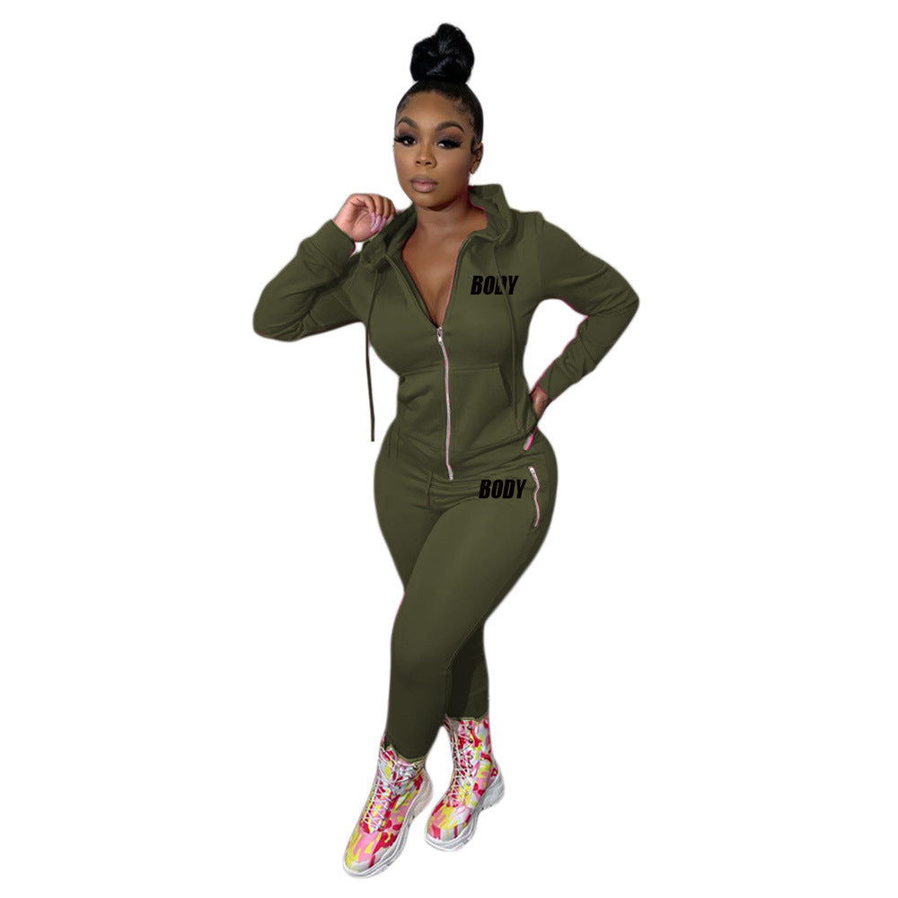 A woman wears an olive green zip-up hooded tracksuit with "BODY" printed in black, featuring pink zipper details.