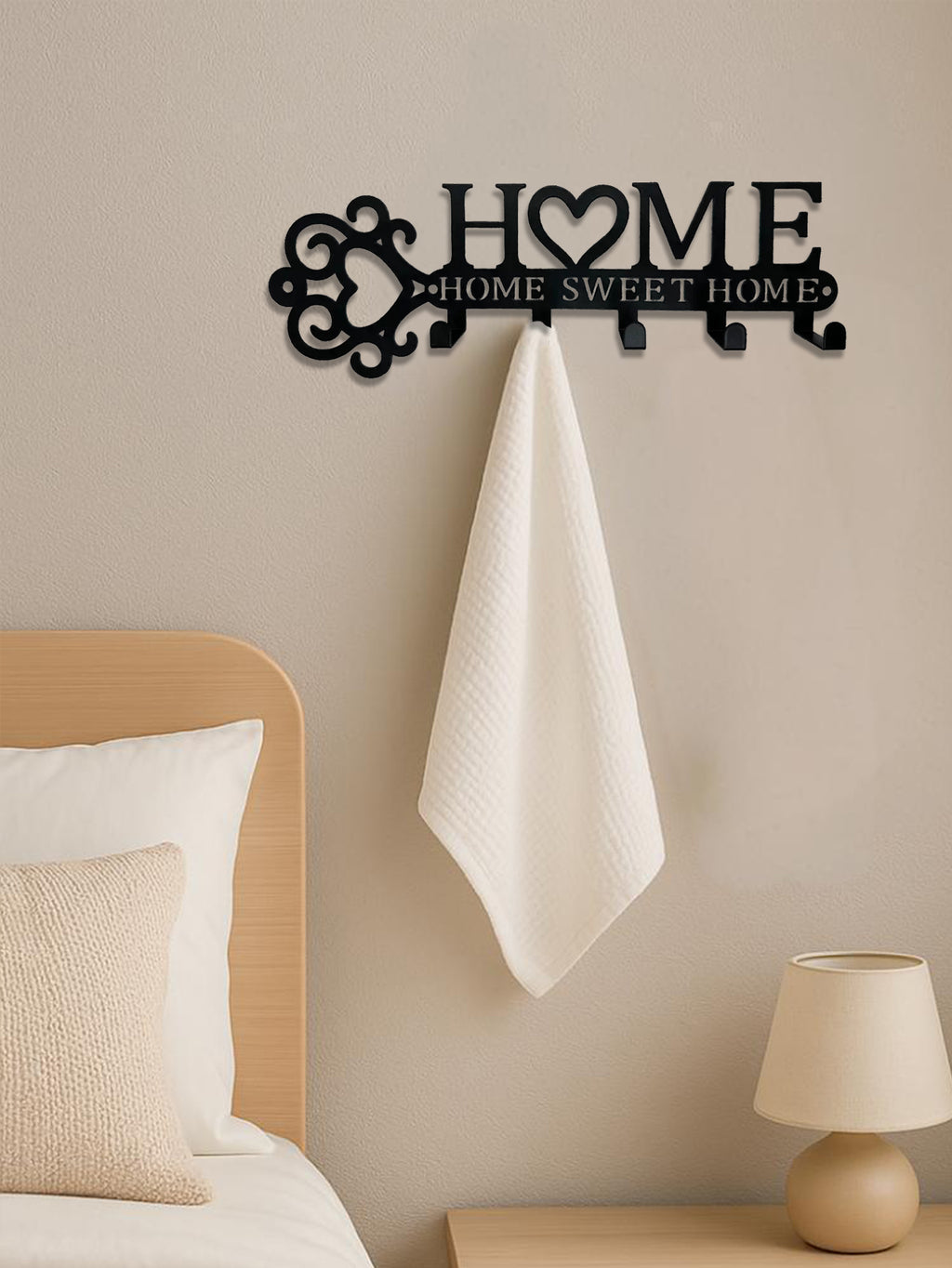 Black metal wall hook set featuring a "HOME" cutout with a heart and towel, mounted on a neutral bedroom wall.