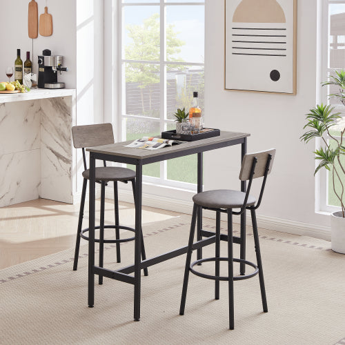 Grey bar table set with two stools featuring padded seats, backrests, and black metal frames in a bright room.