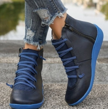 Dark blue flat ankle boots with side zippers, blue laces, and matching blue soles worn with distressed jeans.