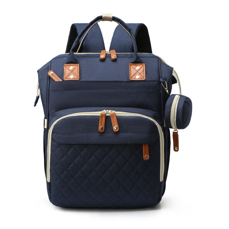Navy blue multifunctional mummy backpack with quilted front pocket, tan leather accents, and integrated USB port.