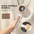 Handheld white and rose gold garment steamer releasing steam, held in a hand against a beige fabric background.