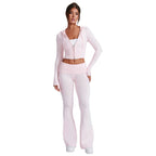 A woman wears a light pink, slim-fit knit hooded zip-up crop top and matching high-waisted flared casual pants.
